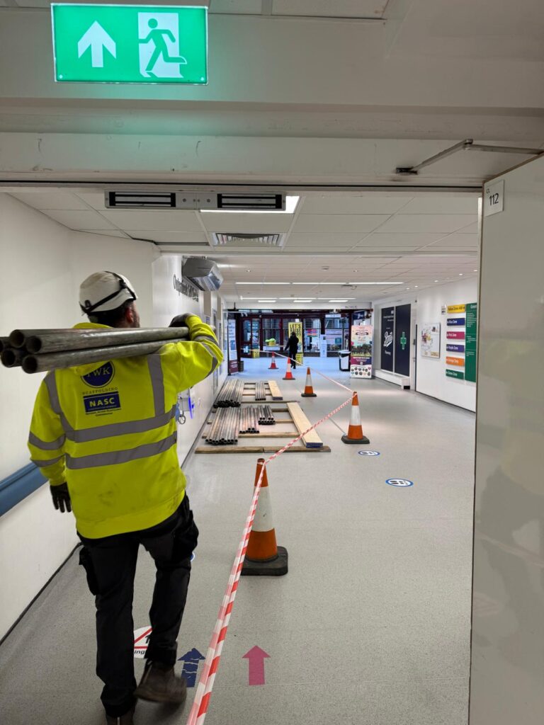 TWK operative fitting scaffold tubes inside a corridor at Poole Hospital