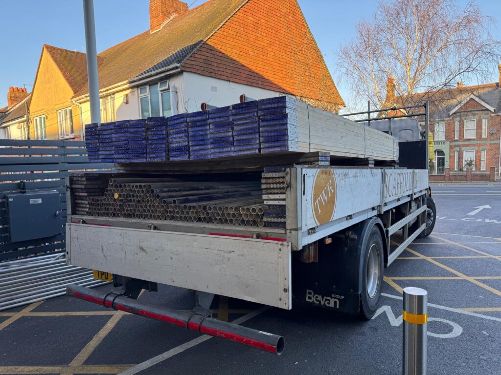 TWK-branded flatbed lorry carrying stacked scaffold tube and boards