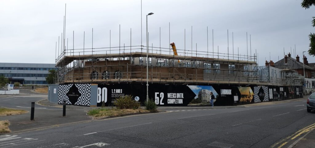 Scaffolding around The Cosmopolitan in Poole, with the named development hoarding in view